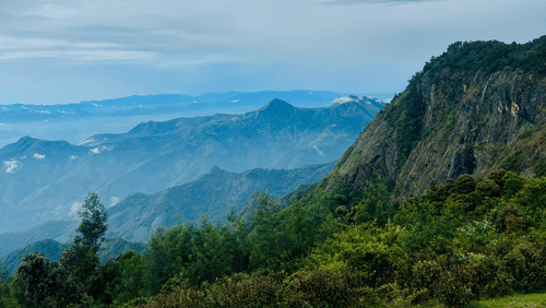 A cliffside view over a misty valley under a cloudy, grey sky.