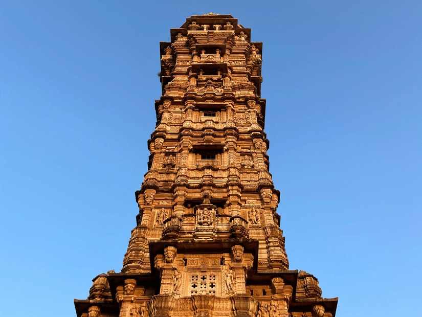 Vijay Stambha rising against clear blue sky, showcasing vertical stone craftsmanship, ornate carvings, and iconic historic monument within fort complex