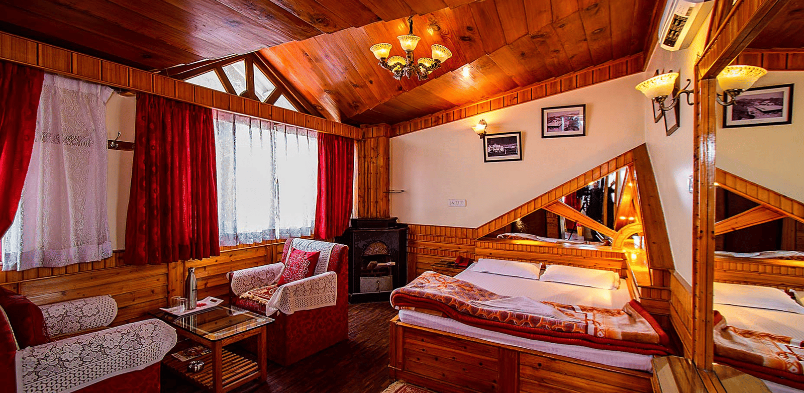 Hotel room with a wooden ceiling, double bed, red and white seating area, and wall mirrors reflecting the room at Hotel Dolphin Darjeeling.