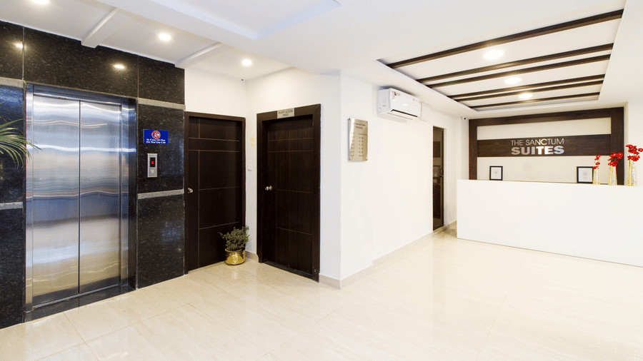 Hotel lobby corridor with a lift, dark wooden panels, and bright white flooring at Sanctum Suites Whitefield, Bangalore.