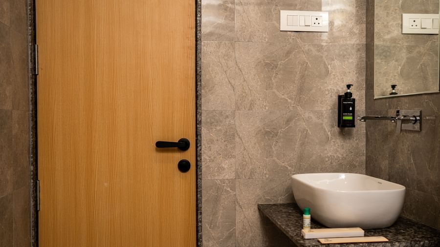 A contemporary bathroom at Daksh The Grand Gowardhan, Dwarka, with a sleek basin and wooden door besides it.