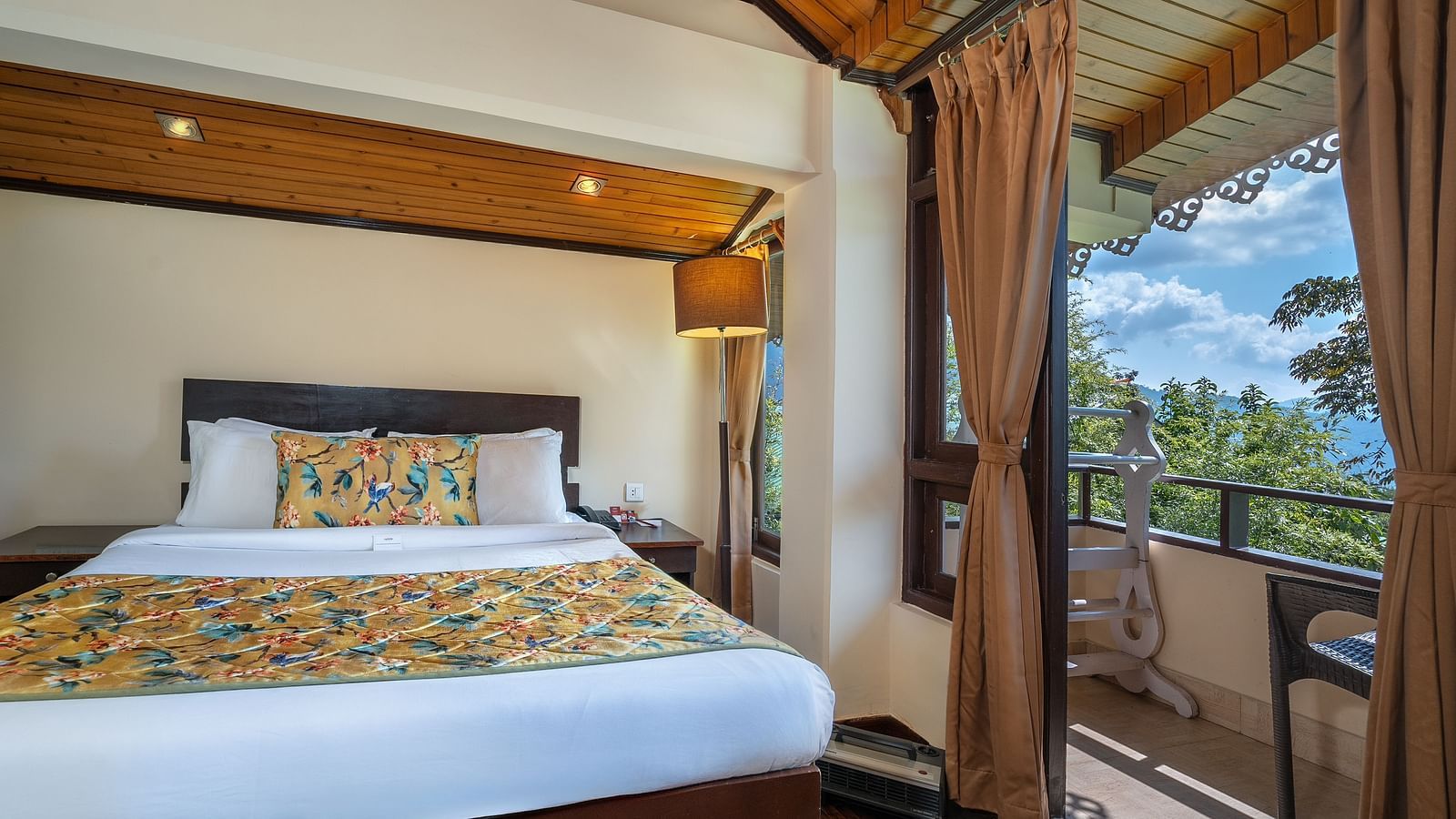 Deluxe room with a spacious bed, wooden bedside table with lamps, and balcony chairs for enjoying the view at Summit Norling Resort & Spa, Gangtok
