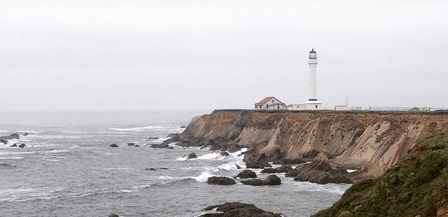 A lighthouse perched on a cliff overlooking the ocean, with waves crashing against the rocky shoreline.