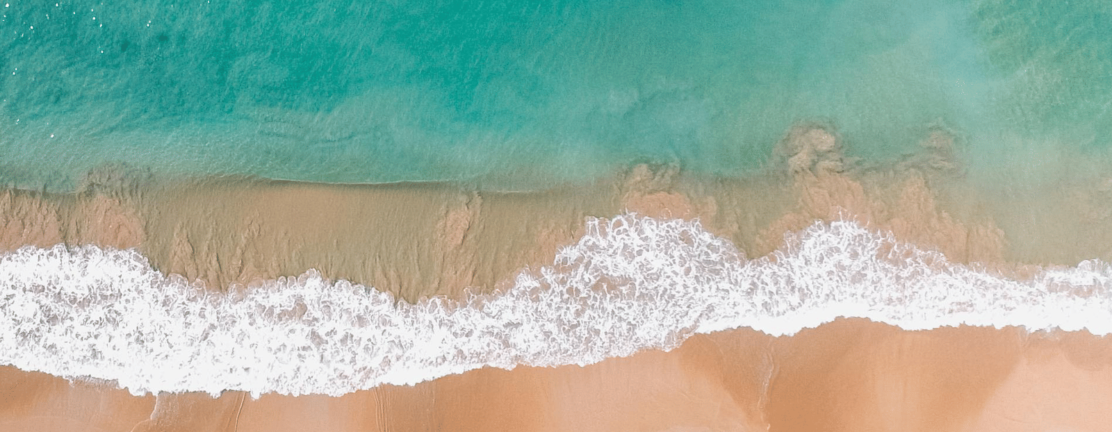 Aerial view of a golden sandy beach meeting turquoise waves along a coastline.