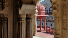 A view through an arched doorway with carved details showing a building with a dome.