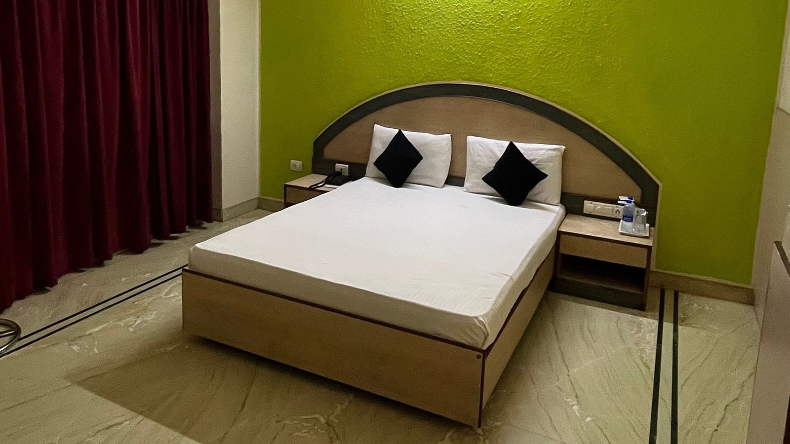 a corner view image of the standard room featuring a double bed against a green coloured wall at The Grand Krishna Rooms, Bengaluru