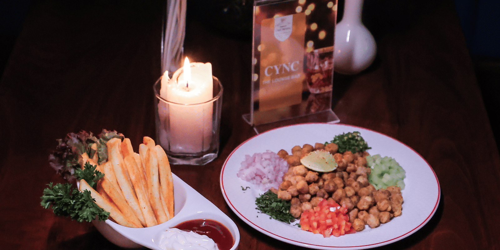 Close-up of small plates of Indian food served with a lit candle and a red rose on a dark table at Hotel Hukam's Lalit Mahal.