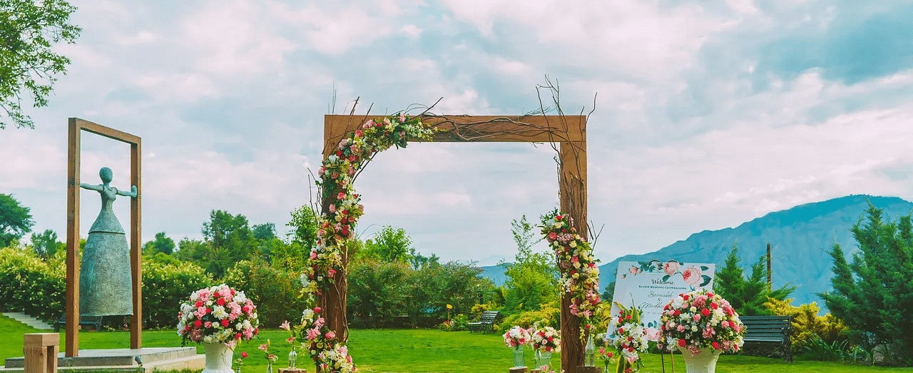 a wooden entrance with flowers decorated on it kept on the manicured grass - neer ganga Resorts