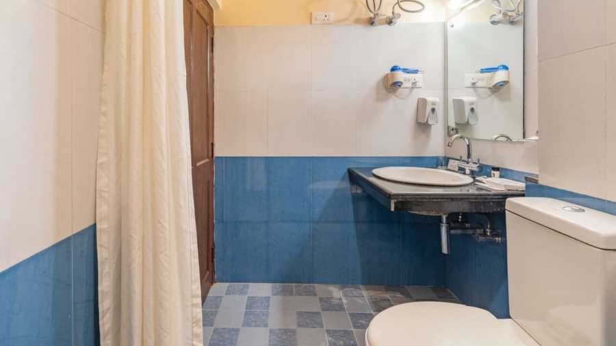 Hotel bathroom with blue and white tiled walls, washbasin with mirror, water heater, toilet, and shower area with curtain - Summit Namnang Courtyard & Spa, Gangtok