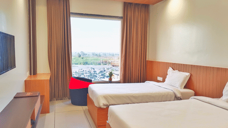 A Superior Twin Room at the Prince ZENQ Xpress Resortt Rohtak with two single beds, a large window offering a view of the outside, light brown wood paneling, and a small red and black chair.