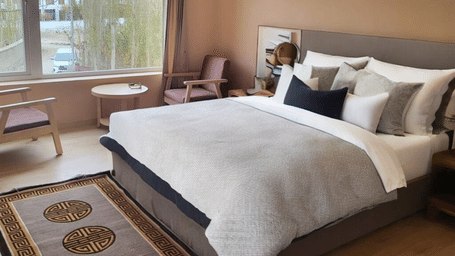 A bright Premium Room at Hotel Dekiling by Eastlynn Collections, Leh, featuring a double bed, seating area by the window, and a traditional rug.