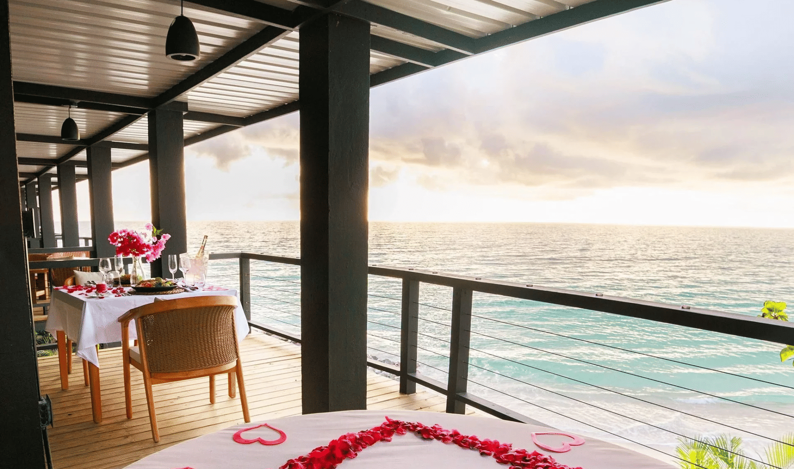 Romantic oceanfront bed adorned with rose petals arranged in a heart shape, set on a terrace overlooking the sea at sunset.