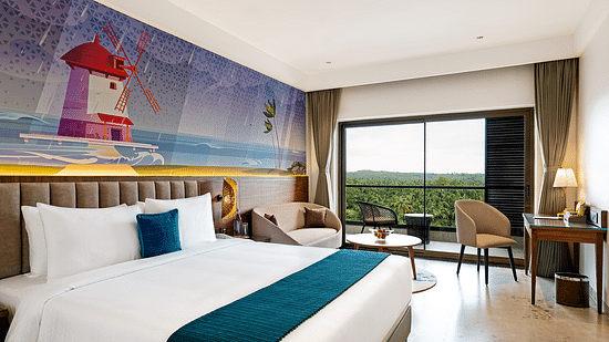 A double bed, seating, and work areas are featured in one of the rooms at Cloud9 Sarovar Premiere, Palolem Goa, with a lighthousing painting on the wall
