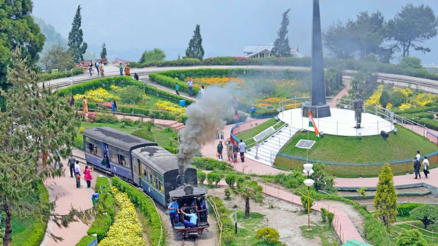 Toy train passing through Batasia Loop garden, with manicured lawns and mountain views.