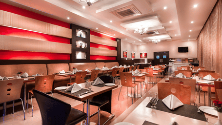 A modern restaurant with bright red and cream-striped walls, wooden chairs, and set tables, at Regency Tuticorin by GRT Hotels.