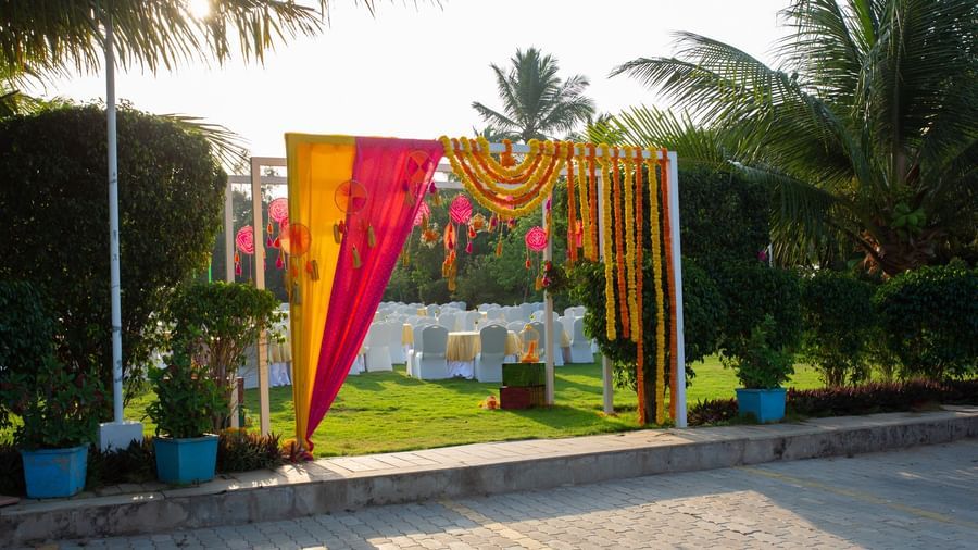 An outdoor event entrance decorated with pink and yellow fabric and marigold garlands, set on a paved area with palm trees  | Citrus Garden | Grand Bay Resort and Spa