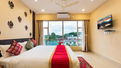 An image of a neatly arranged bed with stylish interior, featuring a wall-mounted TV and a glass window offering a scenic view - Central Courtyard Boutique Hotel, Siliguri