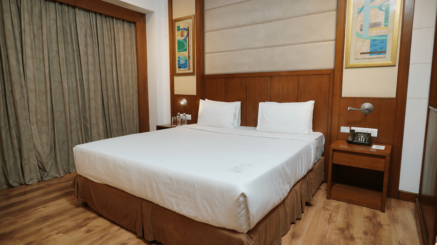 Comfortable deluxe bedroom with a king-size bed, wooden flooring, and modern interiors at Savoy Suites, Greater Noida.