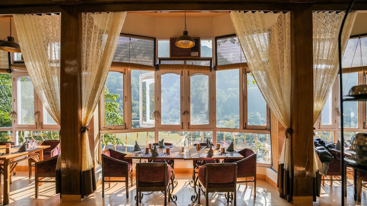 A dining room with a table, chairs, and large windows, warm lighting.