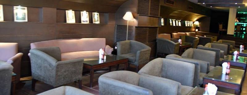 Several grey coloured cushioned arm chairs placed in front of individual tables with a projector hanging from the ceiling at 24 Karats Bar - Hotel Gold, Panipat