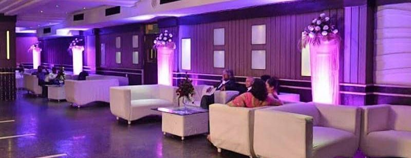 Corner view shot of the 24 Karats bar with people sitting on the sofas and violet halogen lights lit in the corner - Hotel Gold, Panipat