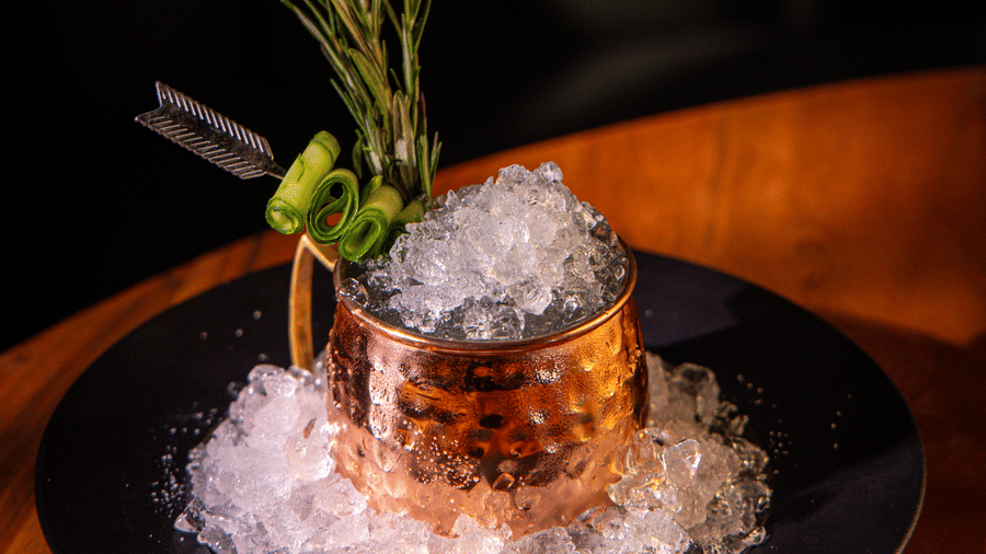 A copper mug cocktail served on a bed of crushed ice, garnished with fresh herbs and a cinnamon stick at Papaya Tree Hotels.