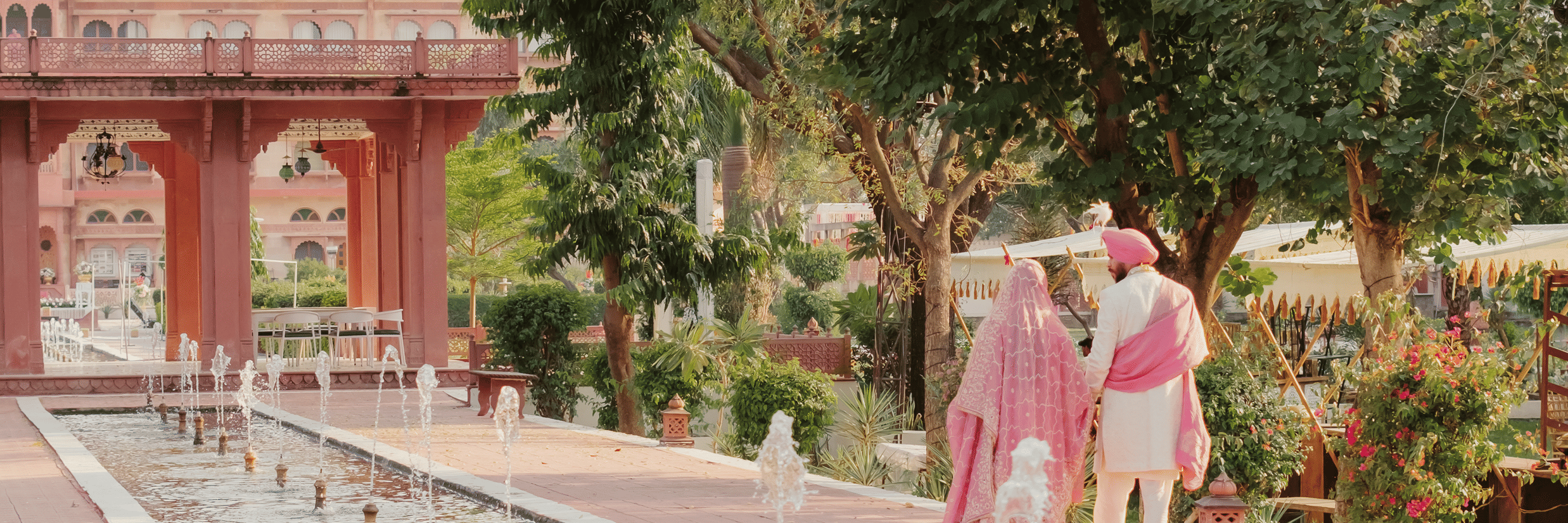 Bride Ritika and groom Jaswinder walking together beside long water garden at Umaid Palace wedding
