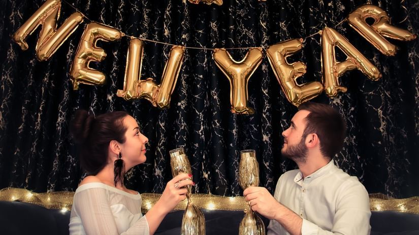 A couple holding drinks with happy new year made out of ballons on the wall