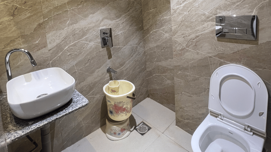 Bathroom of Deluxe Room with Road View furnished with a western commode, a sink, and other bathroom fittings | Daksh The Valley Resort, Saputara