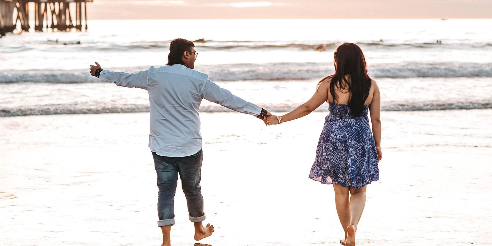 A couple holding hands and walking on the shoreline, basking in the beauty of a sunset over the ocean.