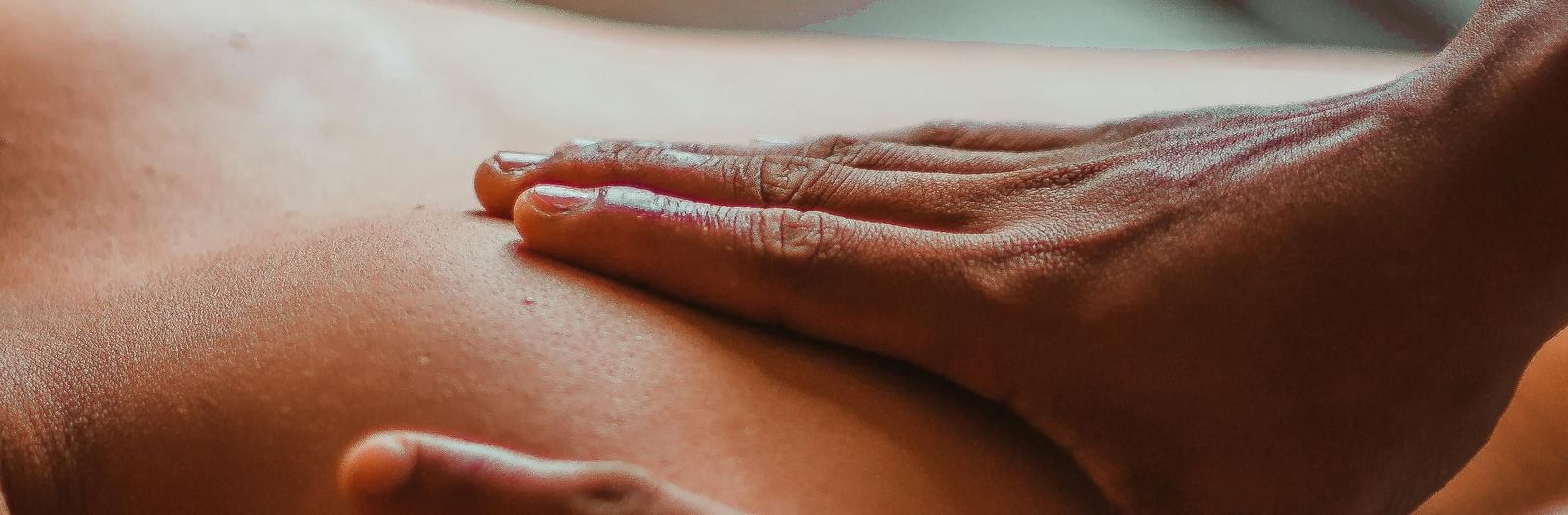 A masseuse is giving a back massage to a person, with both hands on their upper back and shoulders.