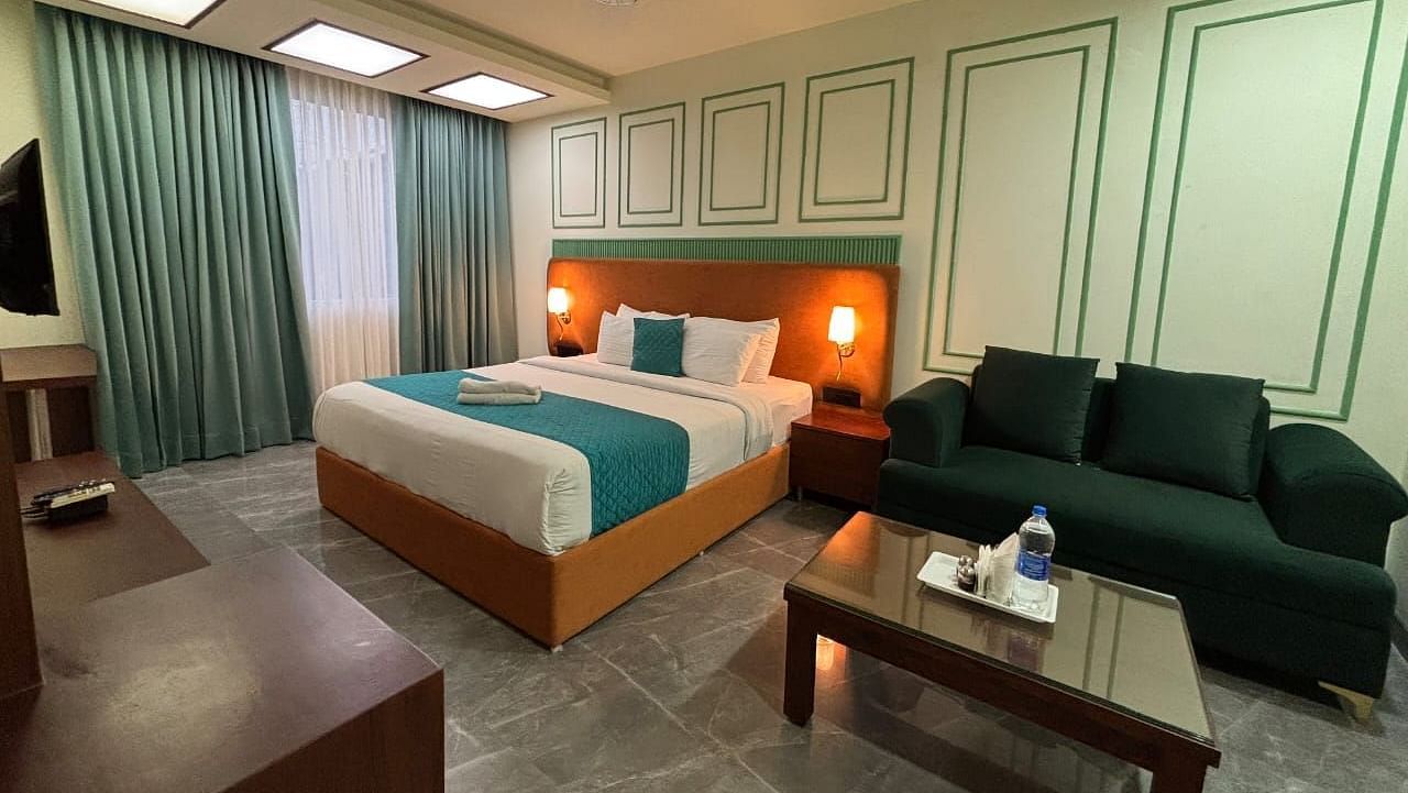 A spacious room with a double bed, a dark green sofa, and a wooden coffee table - Asian Suites IFFCO Metro, Gurgaon