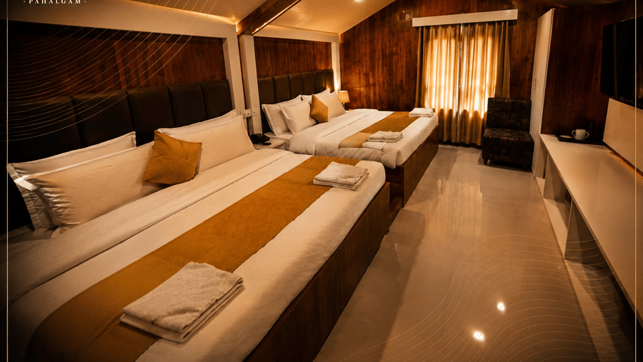 A family room at Hotel Outlook, Pahalgam, featuring 2 double beds placed next to each other along a wall under a sloping wooden ceiling.