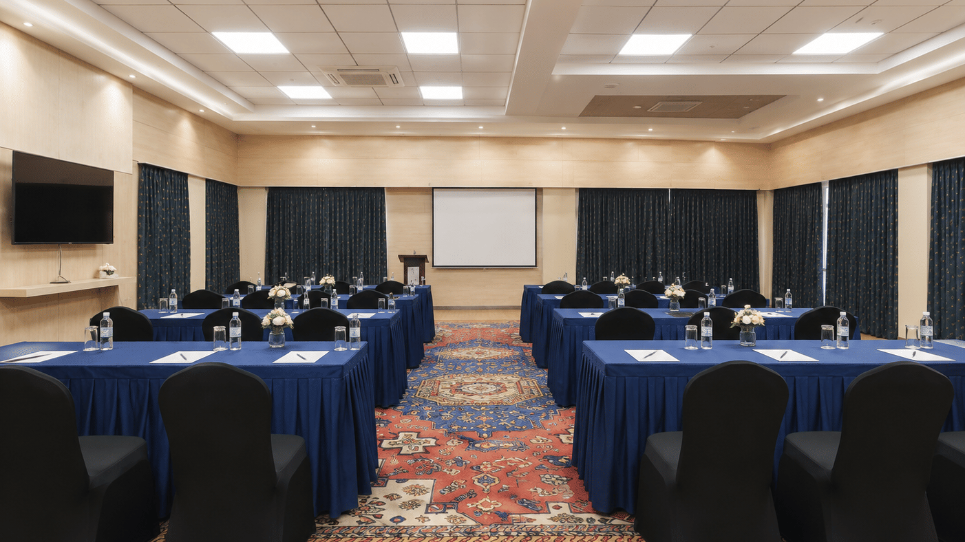 Midfield conference hall in classroom layout with blue-skirted tables, black chair covers and a projection screen at MAYFAIR World Cup Village, Rourkela.