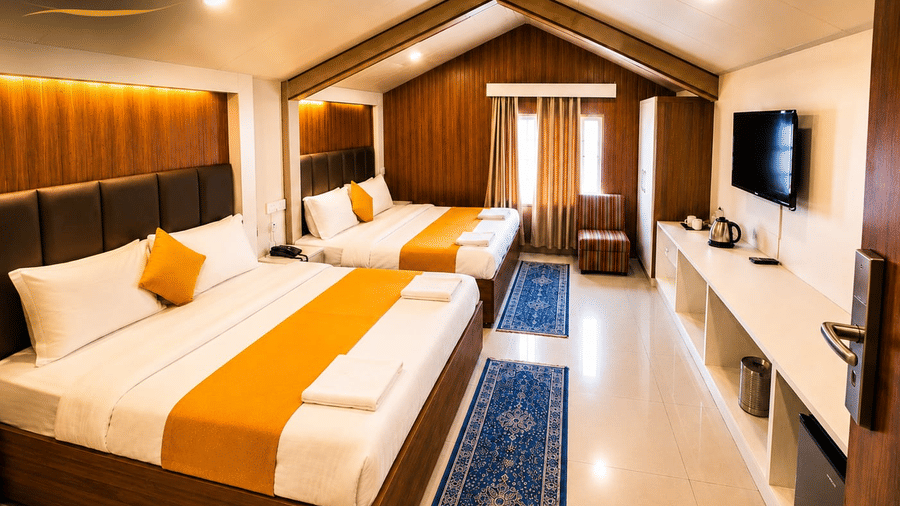 A Family Room at Hotel Outlook, Pahalgam, containing 2 double beds arranged on wooden flooring next to a long storage counter with a television.