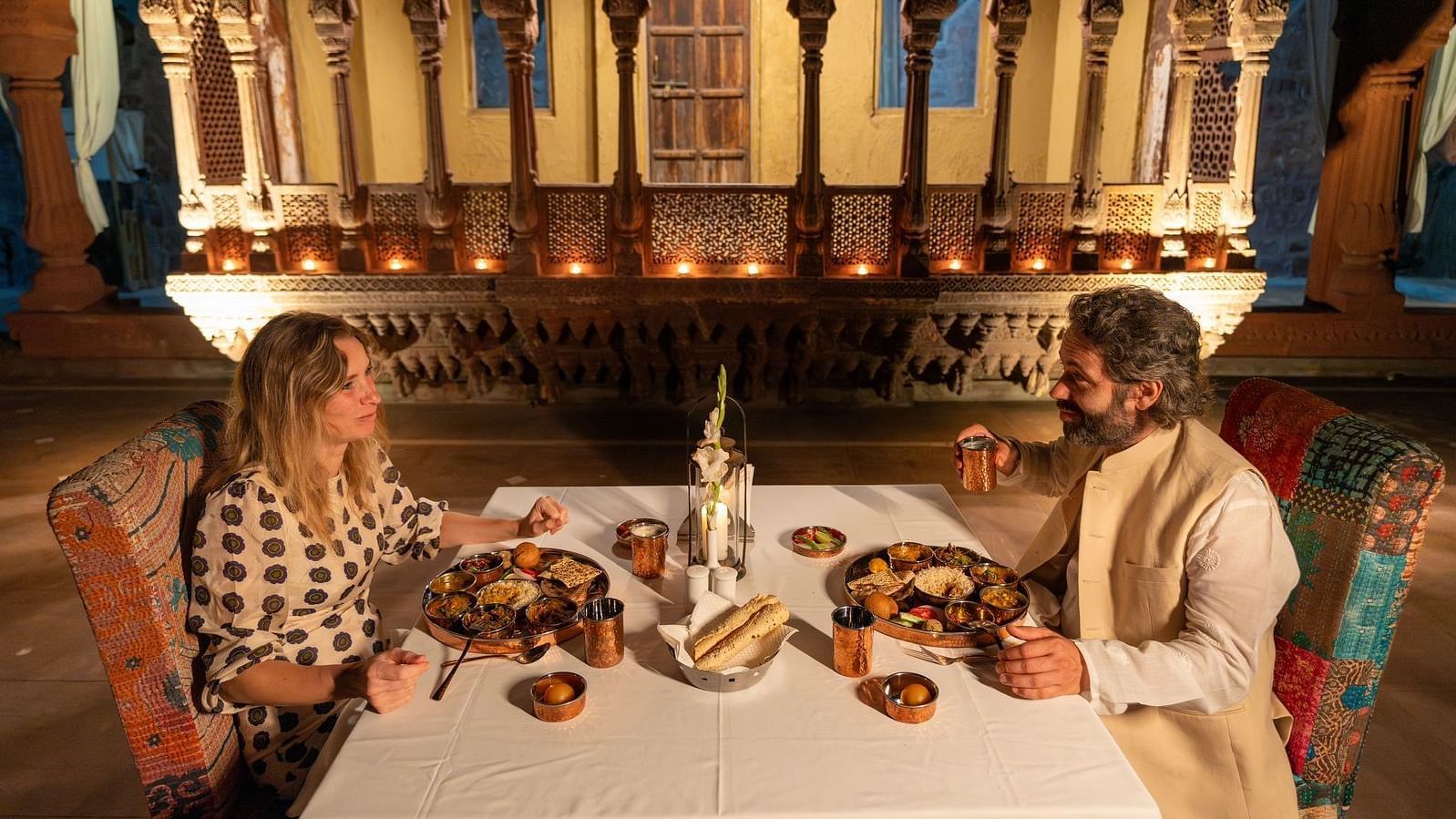 A man and woman in a dining area with an assortment of food placed on the table at Aerial view of a swimming pool with lounge chairs on the side at Surpura Bagh.