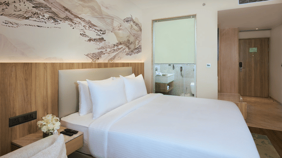 Premium Double Bed Room at Riviera Sarovar Portico, Pathankot, featuring a king size bed, wall-mounted television, wooden flooring, work desk, wardrobe, and an ensuite bathroom.