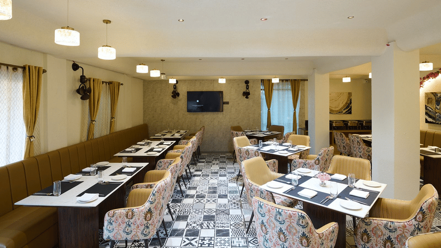 An indoor restaurant dining area with set tables, patterned chairs, and a central TV screen | Voyage Eastin Suites