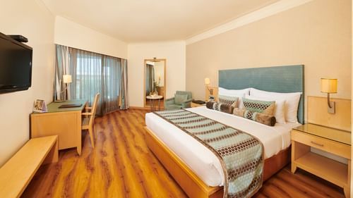 Image of a room at Pride Premier Nagpur featuring a plush bed with cushioned wooden headboard with wooden nightstands on both sides facing the TV mounted on the wall