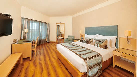 Image of a room at Pride Hotel Nagpur featuring a plush bed with cushioned wooden headboard with wooden nightstands on both sides facing the TV mounted on the wall