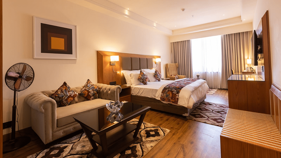 Luxurious hotel room with a king size bed, tufted sofa, glass coffee table, armchair, and a wall-mounted TV - Clarks Inn Express, Ludhiana