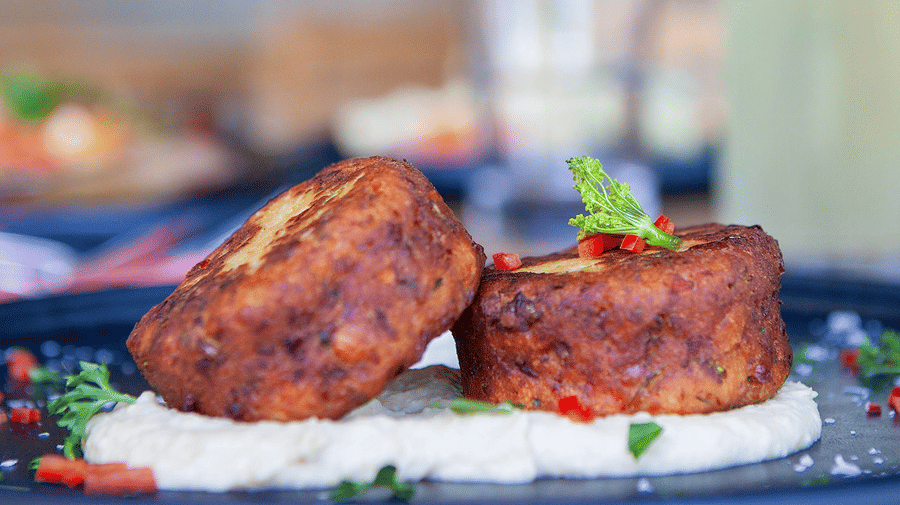 Two patties plated on a creamy puree, garnished with herbs and pepper flakes at YO1 Longevity & Health Resorts
