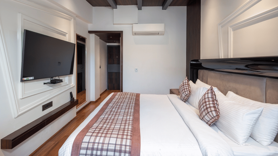 A modern bedroom featuring a bed with white linens, a large flat-screen TV, and an air conditioning unit | Lawrence Solitaire Resort, Nainital