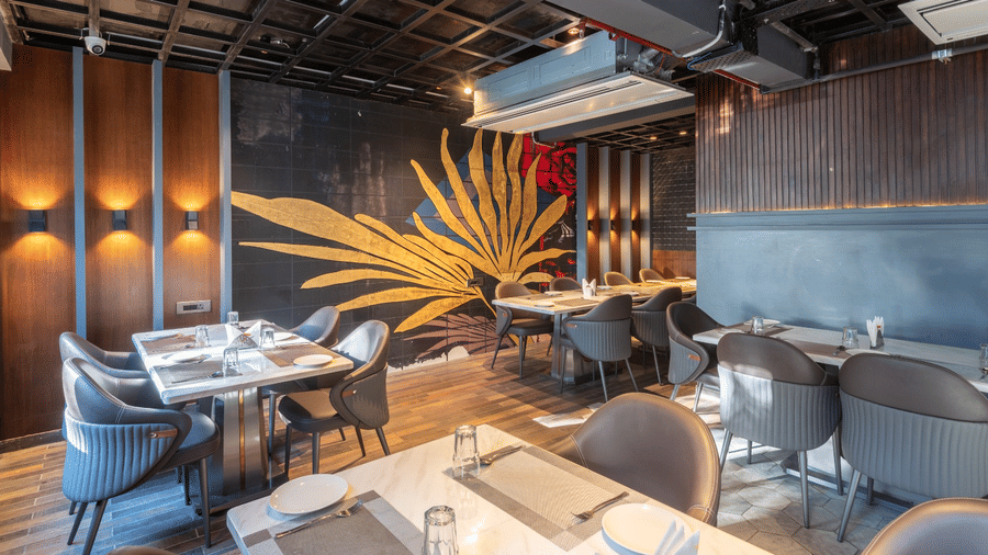 A restaurant interior with dark grey chairs, white tables, and a large golden leaf mural on a dark wall | Lawrence Solitaire Resort, Nainital