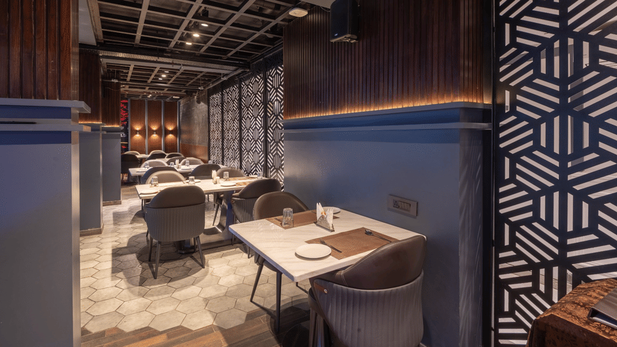 A restaurant interior with dark wooden walls, square dining tables with grey chairs, and a patterned wall section | Lawrence Solitaire Resort, Nainital