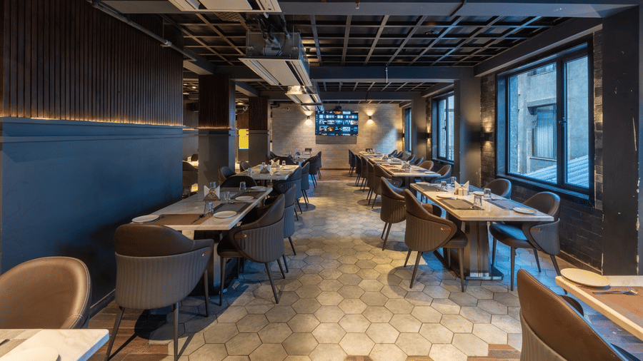 A long view of an indoor restaurant featuring rows of dining tables and chairs alongside large windows | Lawrence Solitaire Resort, Nainital