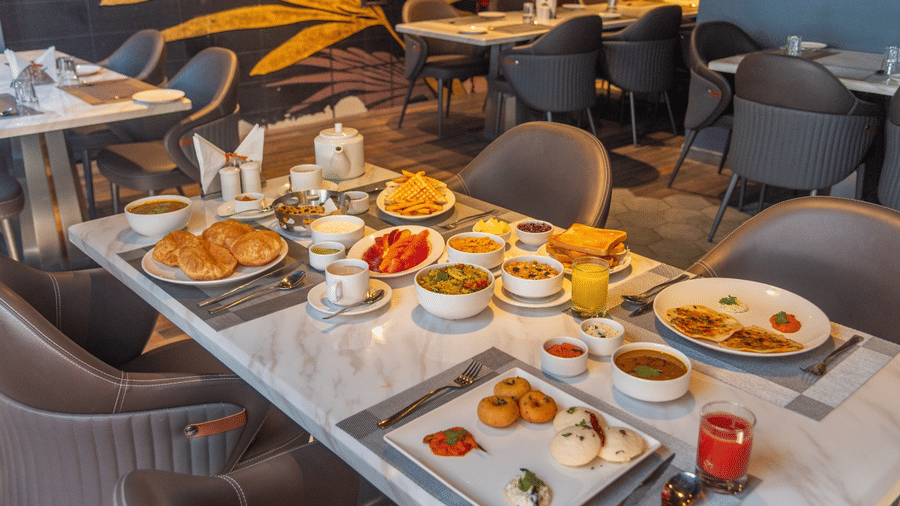 A dining table in a restaurant set with various breakfast dishes, bowls of fruit, and glasses of juice | Lawrence Solitaire Resort, Nainital