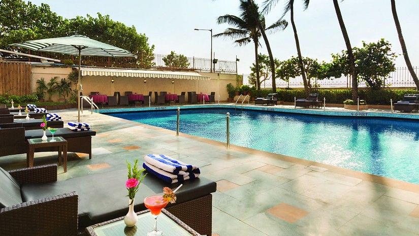 An image of the poolside patio with lounge chairs and palms trees in the background - Ramada Plaza by Wyndham Palm Grove