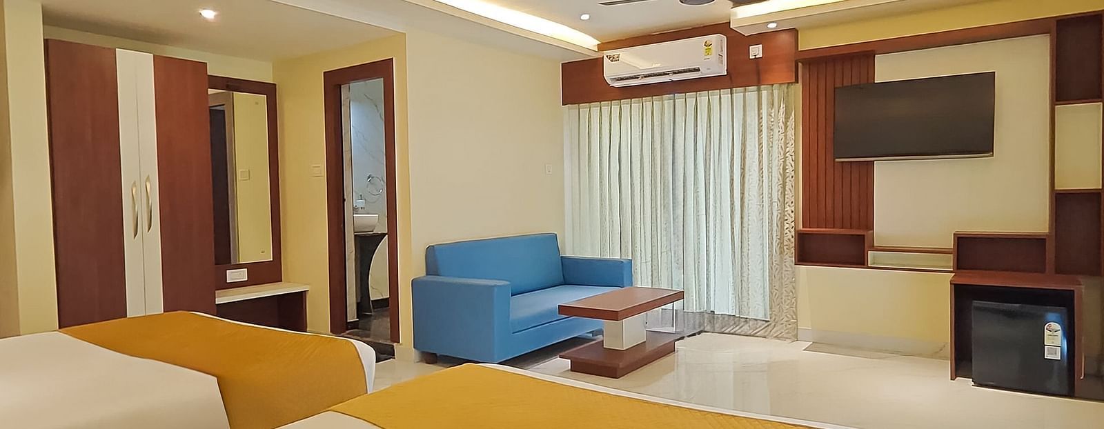 View from two large beds of a seating area, and a TV in a room at Yashshree Bangla Queen, Digha.