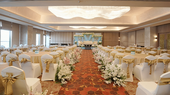 An indoor event space arranged with rows of chairs facing a stage, separated by a central aisle with floral decorations.